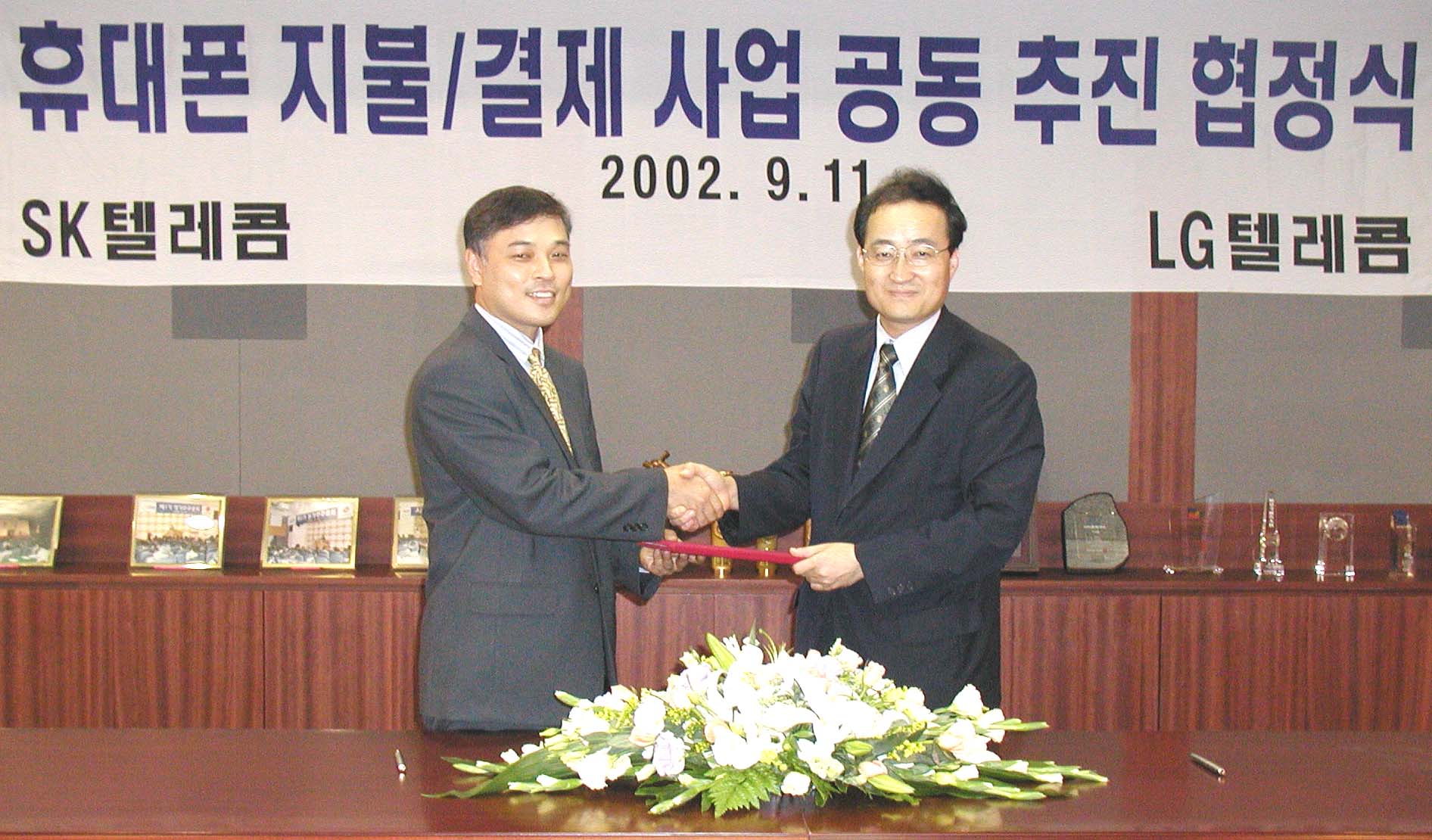 Jin Seuk Cha, managing director of SK Telecom`s m-Finance Division, and Seu Young Nho, managing director of the LG Telecom`s Service Development Office(right), are signing a joint venture agreement in the cellular phone payment/billing business, and shaking hands at LG Kangnam Tour, Yeuksam Dong.